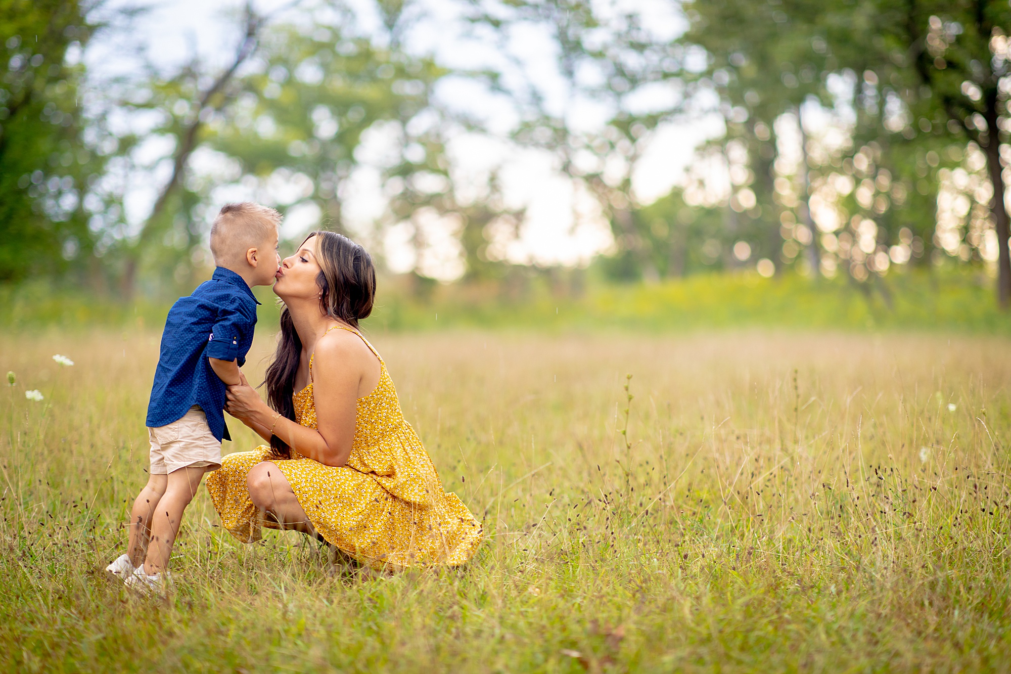 mom kneels down to kiss her son  during family portraits  